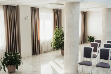 Parlak odada mermer döşeme, uzun pencereler ve bitkilerle minimalist dekorasyon bulunuyor..