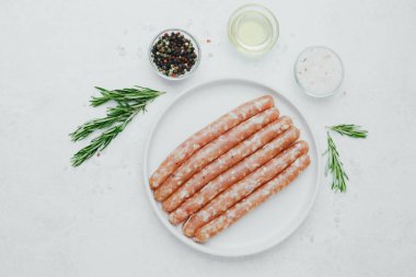 Biberiye ve baharatlı, beyaz tabakta pişmemiş sosisler.