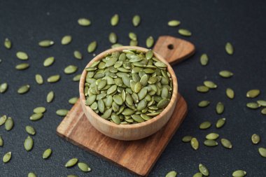 Balkabağı tohumları tahta kasede kesme tahtasının üzerinde siyah arka planda