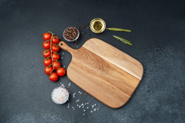 Kiraz domatesli tahta kesmek otlar, tuz ve baharatlar koyu arka planda.