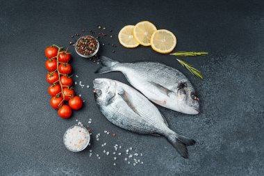 Domatesli taze çiğ dorado balığı limon ve siyah arka planda baharatlar.