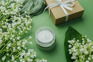 Çiçekli cam kavanoz mumu ve yeşil arka planda hediye kutusu.