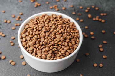 Siyah arka planda kuru köpek mamasıyla dolu beyaz kase ve dağınık mamalar.