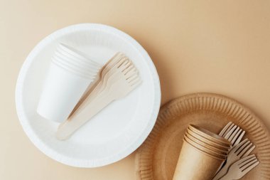 Brown and white disposable paper cups and wooden forks on beige background