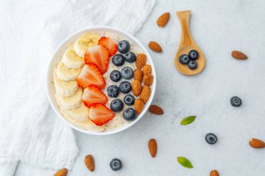 Yulaf ezmesi kasesi, meyve, kaşık ve masaya saçılmış fındık.