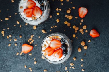 Yoğurtlu granola parfe, koyu arkaplanda çilek ve yabanmersini.