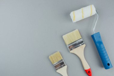 Gri arkaplan üzerindeki boyama araçları arasında ev geliştirme ve iç tasarım konsepti için rulo ve fırçalar da yer almaktadır