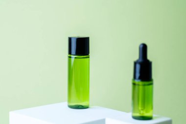 Siyah kapaklı yeşil kozmetik atık şişesi beyaz küp kaide arka planında eşleşen konteynır sergileniyor