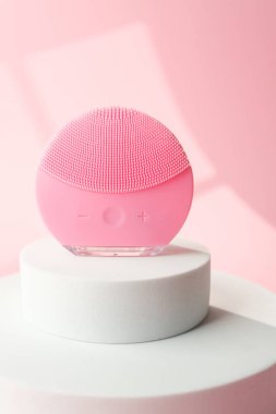 Pembe yuvarlak silikon yüz temizleme cihazı beyaz silindirde duruyor.