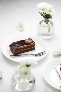 Kremalı pasta dilimi ve çatallı beyaz çiçekler.