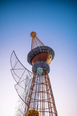 Alacakaranlık gökyüzüne ve ağaçların çıplak dallarına karşı kanatları olan dev ışıklı melek figürü.