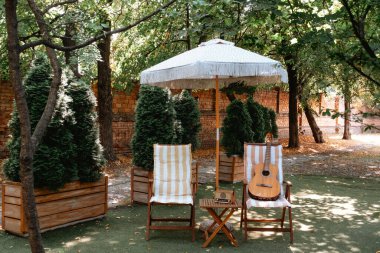 Müzik için güneşli bahçede çizgili sandalyede gitar. 