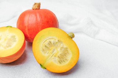 Turuncu balkabağı ikiye bölünmüş. Beyaz kumaş üzerinde turuncu balkabağı olan tohumları gösteriyor.