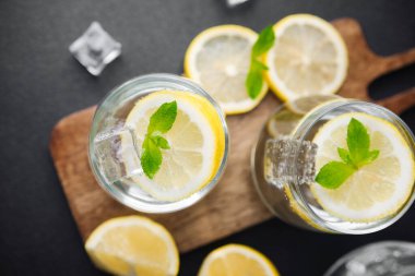 Taze nane yapraklı turunçgil limonatası ve güneşli yaz mutfağında parlak bir masada cam sürahi içinde buz küpleri.