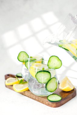 Salatalık limonlu su, tahta tahtada nane, beyaz masada güneş ışığı.