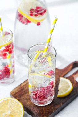 İki uzun bardakta limon kırmızısı üzümlü su ve ahşap tahtada buz küpleriyle pipet.