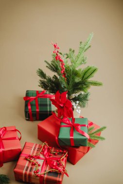 Tarafsız yüzeyde küçük yeşil ağaç ve kırmızı böğürtlenlerle düzenlenmiş Noel hediyeleri.