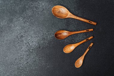 Değişen boyutlarda dört ahşap kaşık. Koyu taşın üzerine düzgün yerleştirilmiş..