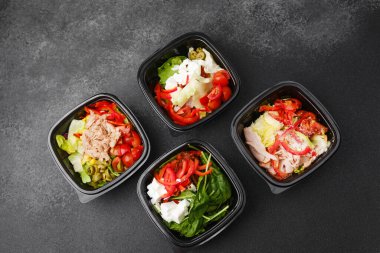 Restoran teslimatı ya da yemek hazırlama konsepti için siyah kaplarda taze sebzelerle karışık salatalar et peyniri ve yeşillikler.