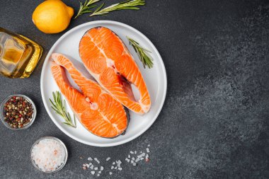 Beyaz bir tabakta somon filetosu, yanında otlar, limon ve çeşitli baharatlar sergileniyor..