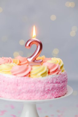 Pembe ve sarı kremalı canlı bir doğum günü pastası. Üzerinde iki numaralı mum var..