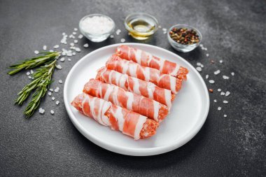 Çiğ domuz pastırması beyaz tabağa sarılmış, baharatlı ve otlu.