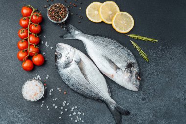 Domatesli taze çiğ dorado balığı limon ve siyah arka planda baharatlar.