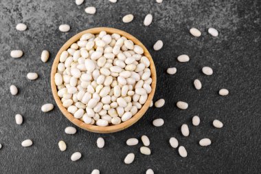 Beyaz fasulyeler, vejetaryen protein, sağlıklı yiyecek veya mutfak düzeni konsepti için siyah taş zemine saçılmış.