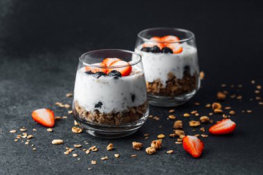 Yoğurtlu granola parfe, koyu arkaplanda çilek ve yabanmersini.