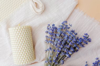 Balmumu çarşaflı lavanta buketi ve kumaş ve pastel arka planda mum.