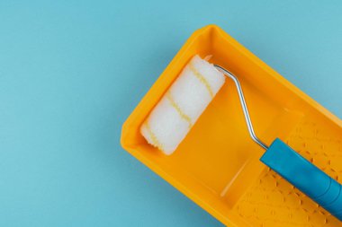 Ev boyama ve yenileme ekipmanları konsepti için sarı tepside mavi renkli boya rulosu.