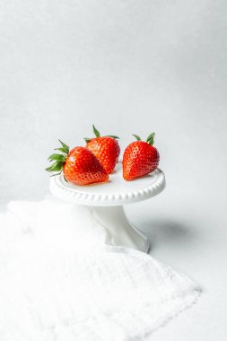 Kırmızı çilekler yumuşak bir arka planı olan beyaz bir pasta standında düzenlenir..