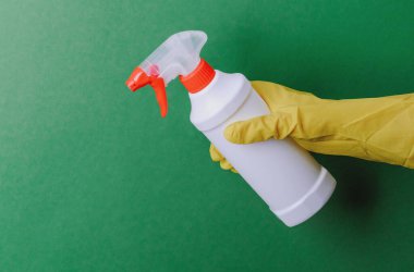 Sarı eldivenli el, yeşil arka planda kırmızı spreyli beyaz sprey şişesini tutuyor..