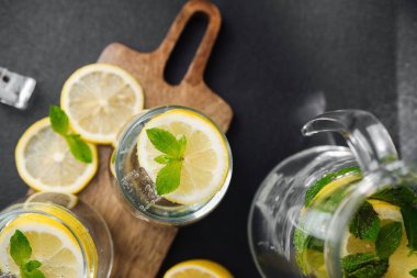 Taze nane yapraklı turunçgil limonatası ve güneşli yaz mutfağında parlak bir masada cam sürahi içinde buz küpleri.