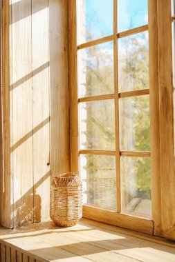 Ilık güneş ışığı, ahşap bir pencereden süzülür ve pervazda örülmüş bir feneri aydınlatır..