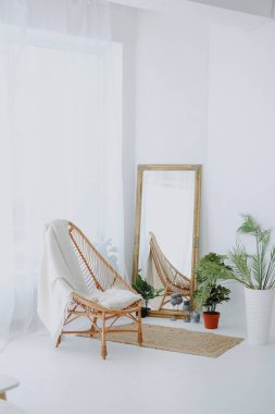 Uzun aynanın yanında battaniyeli örülmüş sandalye ve parlak beyaz odada yeşil bitkiler.