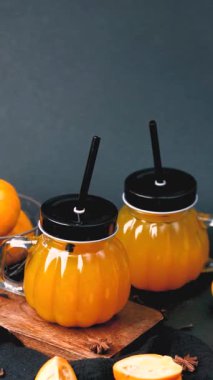 Meyve suyu dolu portakal kabağı şeklindeki bardaklar, siyah bir masada pipetle servis edilir..