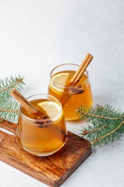 Tarçın çubuklu sıcak içecekler, limon dilimleri, yıldız anason ve tahta üzerinde çam iğneleri.