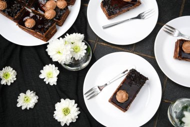 Kremalı lezzetli çikolatalı kekler ve siyah kumaş ve tabakta çiçekler.
