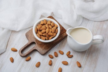 Badem sütü beyaz sürahide badem de ahşap tahtada kâsede, açık masa arka planında