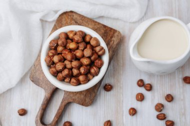 Tahta tahtada bir sürahi bitkisel sütle bir kase fındık.