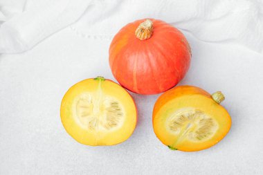 Parlak turuncu balkabağı ve yarımlar temiz beyaz yüzeyde parlak sarı et ve tohumlar gösteriyor..