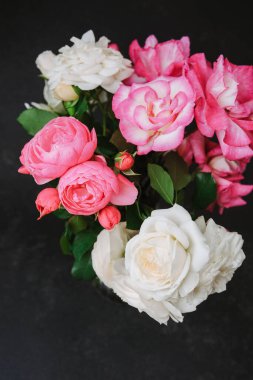 Canlı pembe ve beyaz güller koyu desenli bir yüzey üzerinde cam bir vazoda dizilmiş..