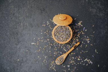 Ahşap bir kasede kurutulmuş lavanta çiçekleri ve koyu arka planda kaşık..