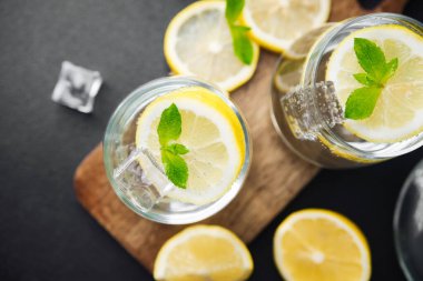 Taze nane yapraklı turunçgil limonatası ve güneşli yaz mutfağında parlak bir masada cam sürahi içinde buz küpleri.