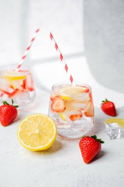 Parlak masada servis edilen buz küpleri ve çizgili kamışlarla berrak bardaklarda çilekli limonlu su.