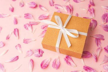 Dağınık şakayık yaprakları ve pembe gruplaşmış beyaz kurdeleli hediye kutusuna yakın çekim.
