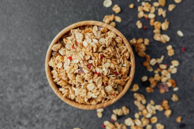 Üst manzara granola kasede, koyu arkaplanda dağınık parçalar var.