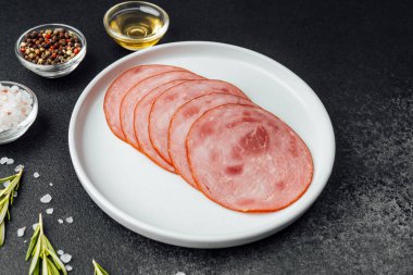 Yuvarlak dilimlenmiş sosis tabakta otlar ve baharatlar siyah masada