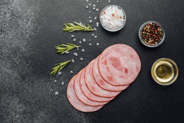 Koyu taş yüzeyde baharatlı ve otlu jambon dilimleri.